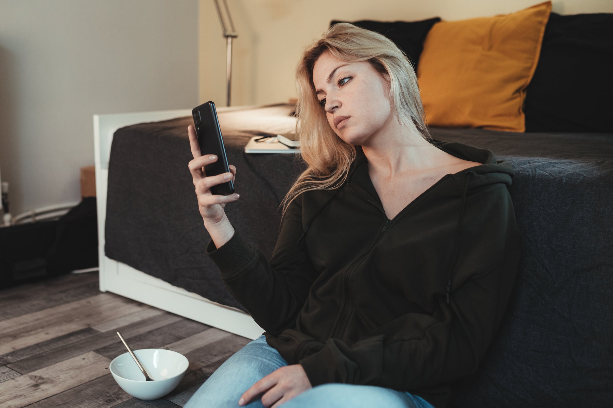 vrouw zittend op de grond kijkend op haar telefoon